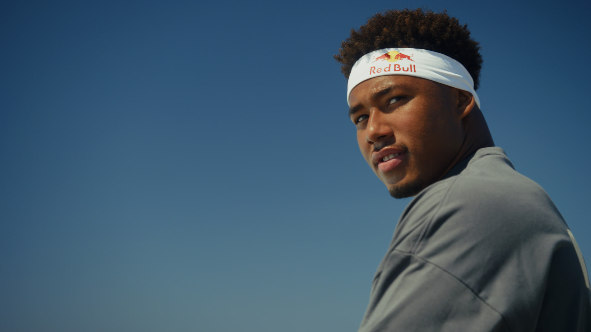 Athlete in a Red Bull headband looking back over his shoulder against a clear blue sky