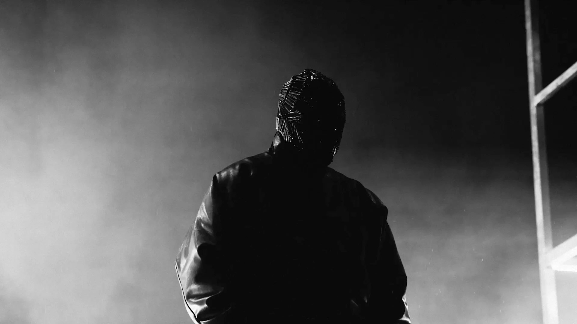 Masked figure in a leather jacket standing in rain and smoke, black and white